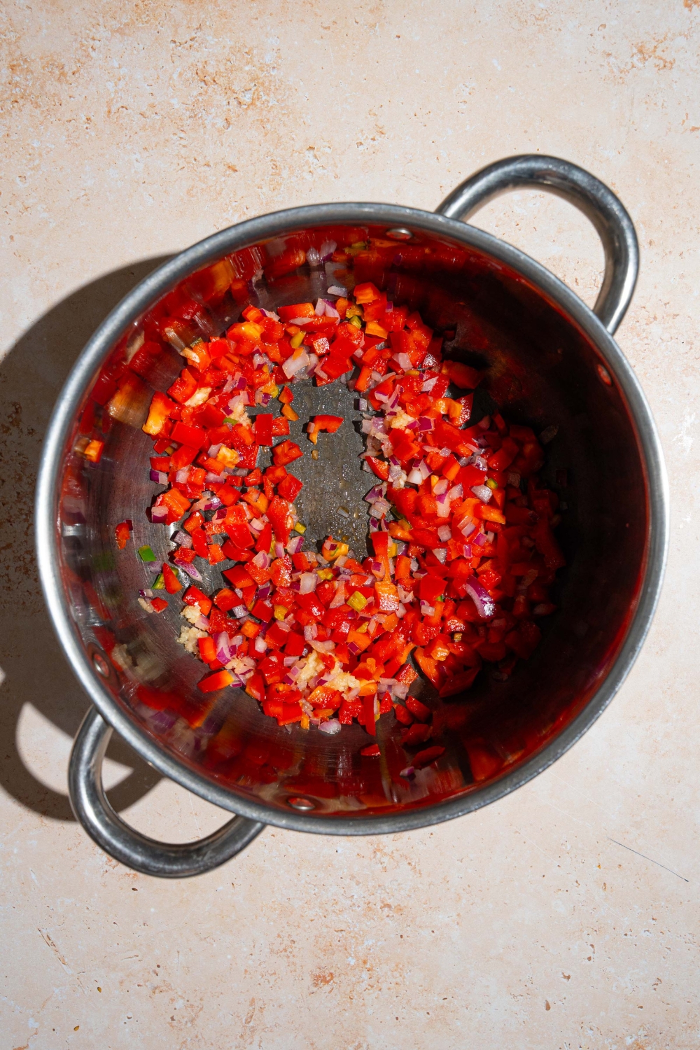 A stock pot with diced pepper, onion, garlic, and jalapeno sautéing in oil. The pot is on a tan counter.