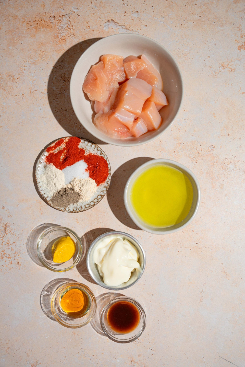 An overhead shot of several bowls in various sizes containing ingredients to make copycat Chick Fil A nuggets including chicken breast, dill pickle juice, mayo, mustard, BBQ sauce, honey, and spices.