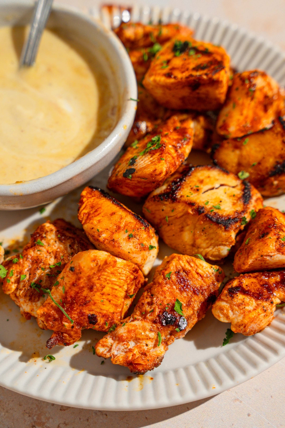 A white plate with homemade Chick Fil A nuggets garnished with fresh parsley. There is a bowl of dipping sauce on the plate with a spoon in the sauce.