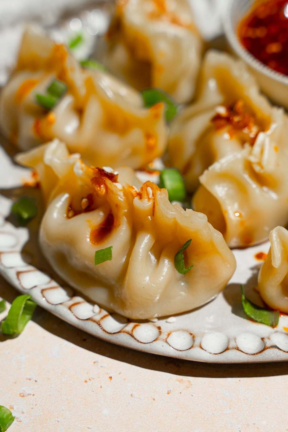 A white plate with steamed chicken dumplings garnished with sliced green onion. The plate is on a tan counter.