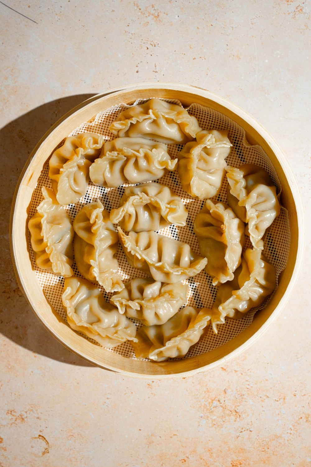 A steamer basket with steamed chicken dumplings. The basket is on a tan counter.