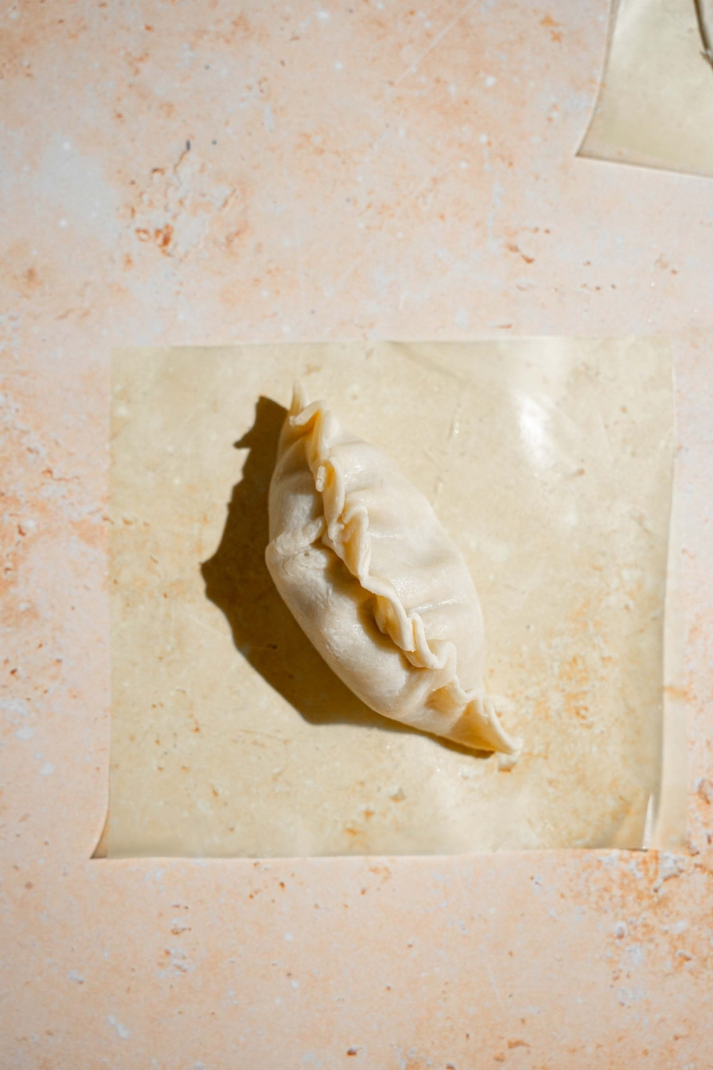 A wrapped chicken dumpling on a piece of parchment paper on a tan counter.