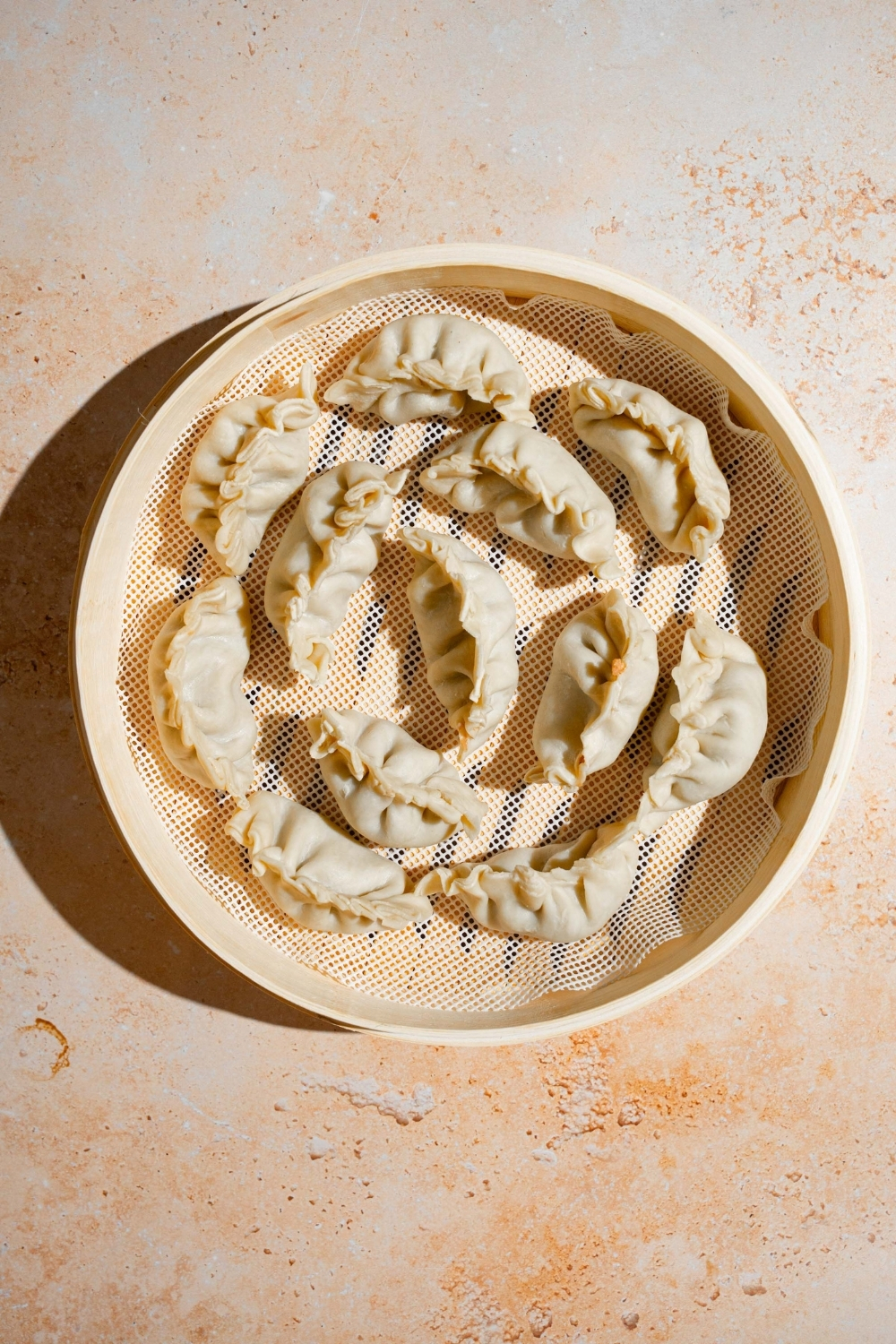 A steamer basket with wrapped chicken dumplings. The basket is on a tan counter.